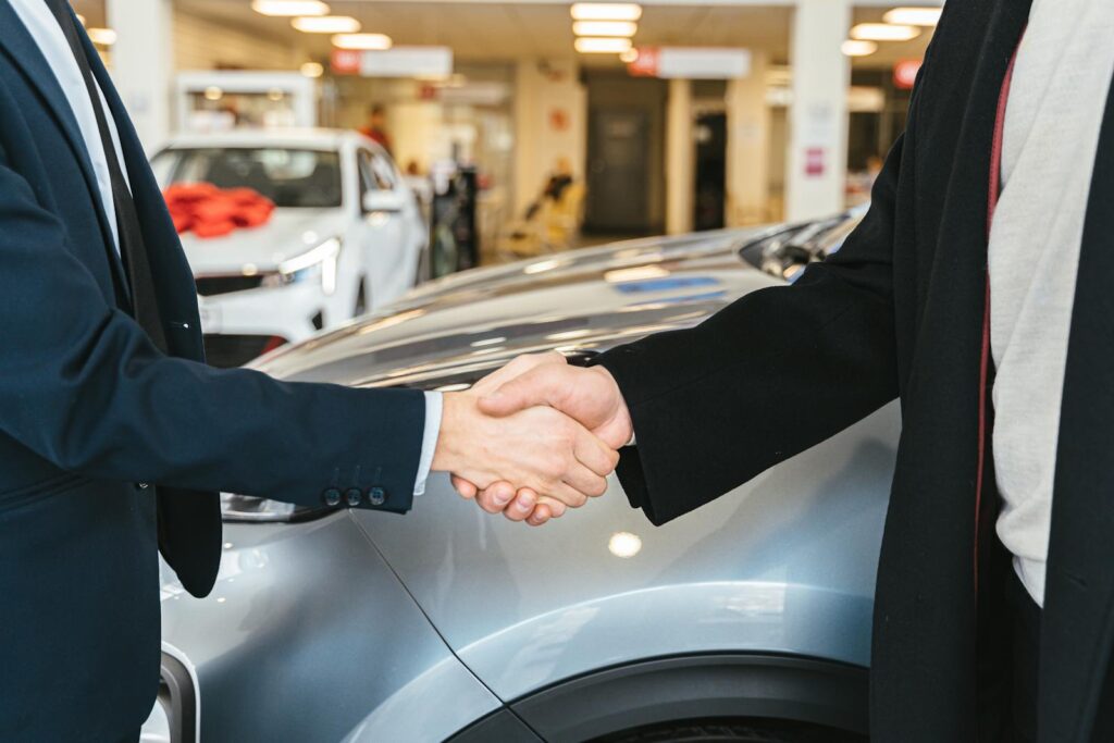 Two businessmen shaking hands in a car dealership, sealing a deal.